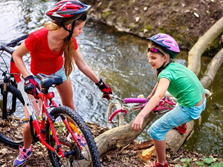 Obraz premium Bikes bicycle girl. Children with bicycle to help each other to cross river on log. Girl rides bicycle. Girl bicycling fording throught water . Bicycle trip is good for health.
