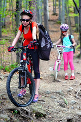 Plakat Bikes bicyclist girl. Girls wearing bicycle helmet and glasses with rucksack rides bicycle. Girls children are bicycling in summer park. Biking is good for health.