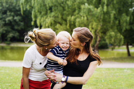 Two women kissing toddler boy in park