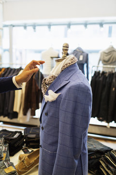 Cropped image of designer's hand reaching mannequin in clothing store