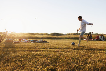 Man holding beer bottle while playing soccer at picnic
