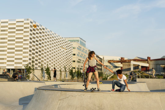 Teenage girl assisting friend in getting up at skate park