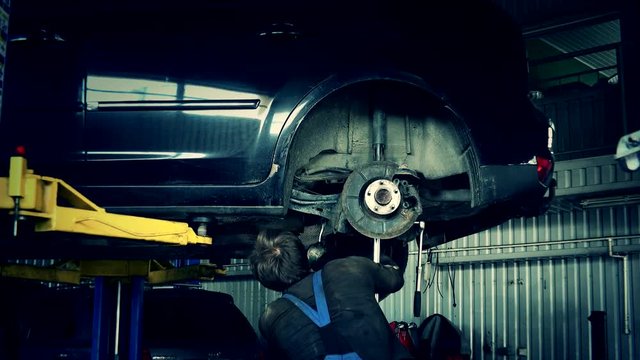 Specialist Guy Working Under Lifted Car In Garage.