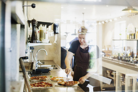 Female chef cutting pizza in commercial kitchen