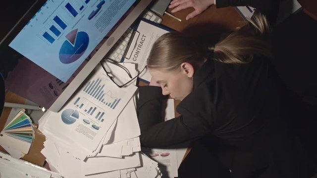 Directly above tracking shot of exhausted young businesswoman sleeping on desk surrounded by piles of documents in dark office, taken on Sony NEX700 + Odyssey 7Q