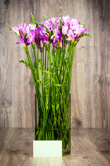 Freesia flowers in the vase on wooden background