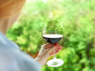 Woman holding glass of wine on blurred natural background