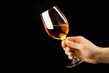 Naklejka na ściany i meble Male hand holding glass of wine on black background
