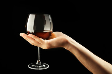 Fototapeta na wymiar Male hand holding glass of wine on black background