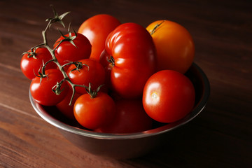 Different tomatoes in metallic bowl on wooden background