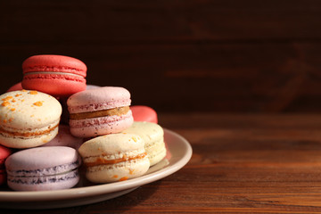 Tasty macaroons in white plate on wooden background
