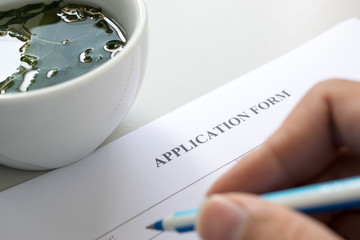 teacup and hand with pen over application form