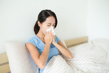 Asian woman sneezing on bed