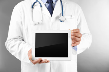 Professional doctor with tablet on grey background