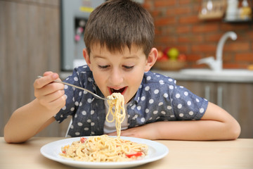 Cute boy eating spaghetti on kitchen