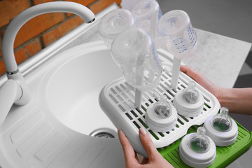 Woman hands holding plastic drying rack with baby bottles