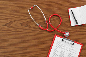 Red stethoscope with clipboard on wooden table