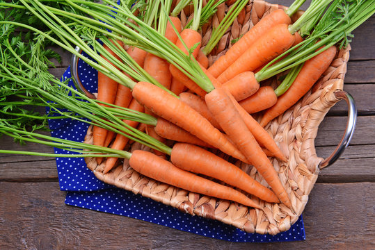 Fresh carrots in wicker tray on wooden table