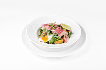 Salad with tuna, lettuce, tomatoes, eggs and potatoes on a plate on a white background