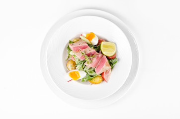 Salad with tuna, lettuce, tomatoes, eggs and potatoes on a plate on a white background, top view