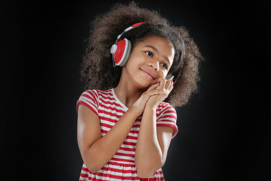 Afro-American little girl with headphones on dark background