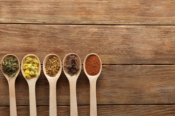 Dried healing herbs and seeds in spoons on wooden background