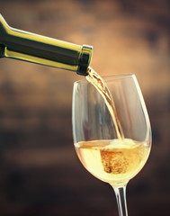 White wine pouring in glass on brown background