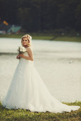 Fototapeta na wymiar Pretty blonde bride stands on the lake shore in a shiny day