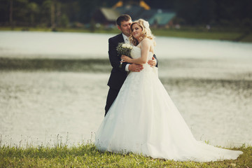 Bride and groom hug each other standing on a lake shore