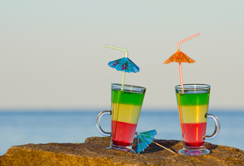 Two cocktails with straws standing on a rock against the sea