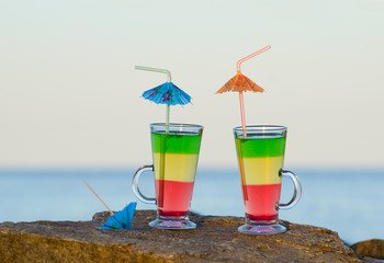 Two cocktails with straws on a rock near the sea