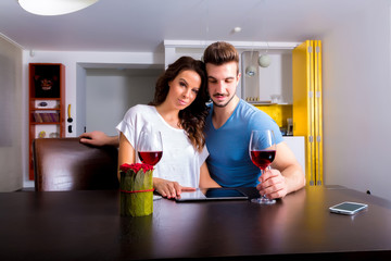 Young couple using a Tablet PC while having a glass of wine