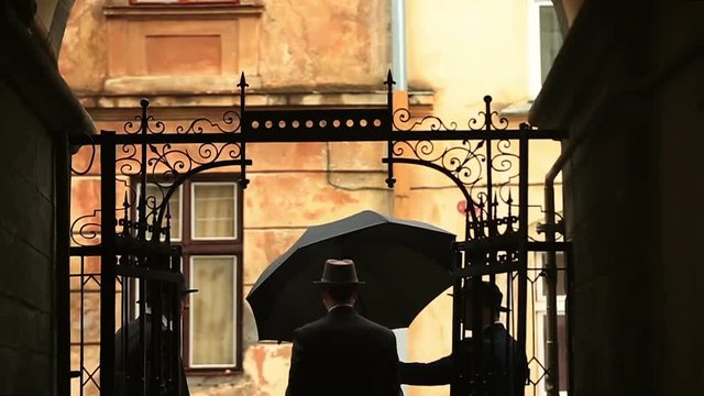 Silhouettes of three gentleman in a hats and vintage suits waiting near fancy metal door smoking and walk away