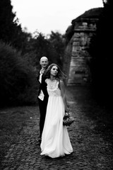 Fototapeta na wymiar Bride walks along the pass in the park holding groom's hand