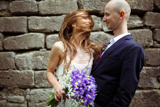 Bride mixes her hair around her face while groom holds her