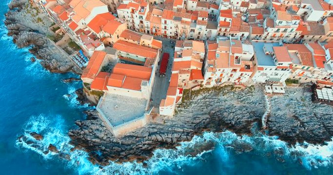 Descending over house roofs and rocky beach in historic town 