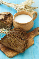 Homemade bread, milk and ripe ears of wheat on a blue wooden bac