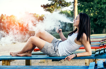 Naklejka premium Long hair brunette girl smoking electronic cigarette on the beac