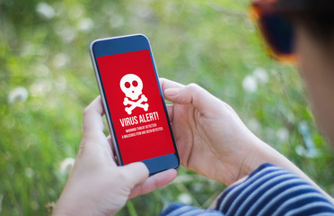 girl in grass holding her smartphone with virus alert