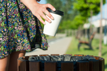 Close-up female hand throwing paper cup on trash
