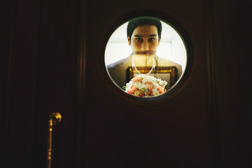 Man with a bouquet of roses looks through the round window in a