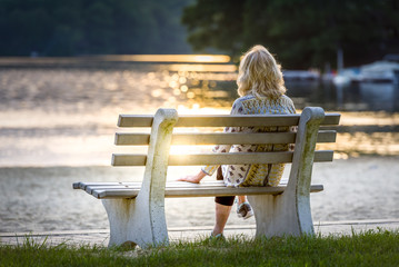 Woman sitting on a bench watching the sun set at a lake on the beach