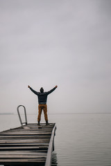 Fototapeta premium Man standing on a old wooden dock with raised hands
