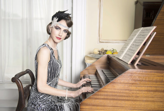 Pretty brunette in twenties theme sequinned dress sitting at harpsichord making eye contact with a nice smile