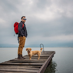 Man and his dog standing on wooden dock - obrazy, fototapety, plakaty
