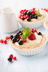 Homemade Tartlets with cream and fresh berries - ripe red and black currants, strawberries on blue rustic wooden table, selective focus