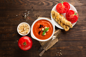 Tomato cream soup with baked tomatoes, red pepper, herbs and spices on dark rustic wooden background, selective focus