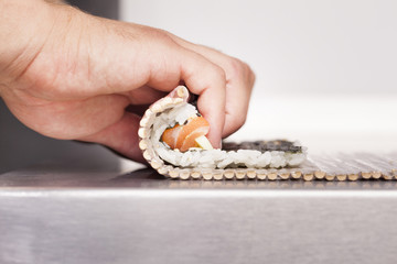 Sushi master turns sushi rolls on a stainless table