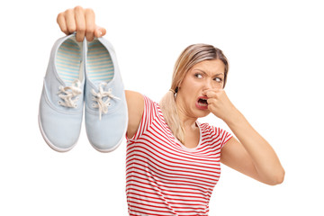 Disgusted woman holding stinky shoes