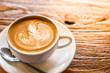 cup of the latte art coffee with spoon and plate on the brown bark beautiful texture background with warm light